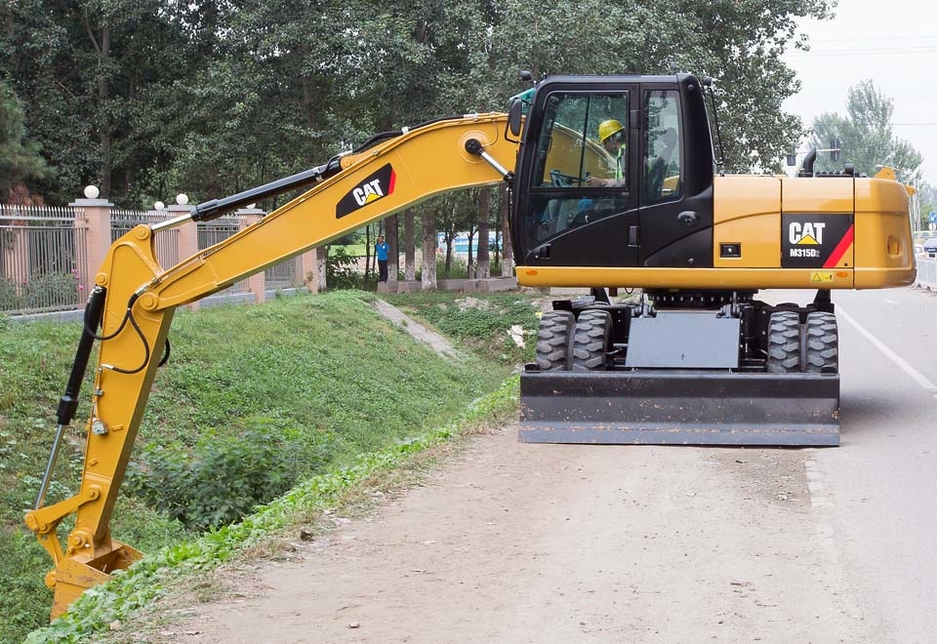 A Cat M315D2 wheel excavator performs work activities on an on-road site. A Cat M315D2 wheel excavator performs work activities on an on-road site.