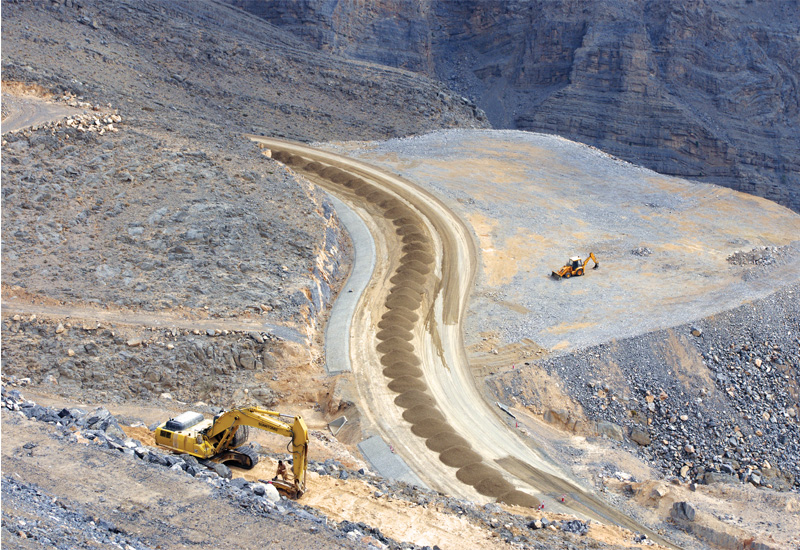 Piles of aggregate waiting to be compacted that have been trucked from the crusher at the top of the hill. To the right, a JCB sits on a plateau creat Piles of aggregate waiting to be compacted that have been trucked from the crusher at the top of the hill. To the right, a JCB sits on a plateau creat